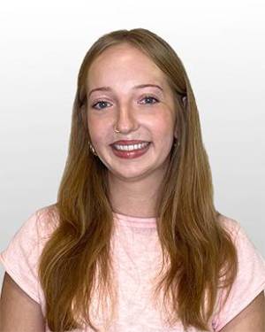 Shelby Crowley smiling in a pink shirt against a gray background